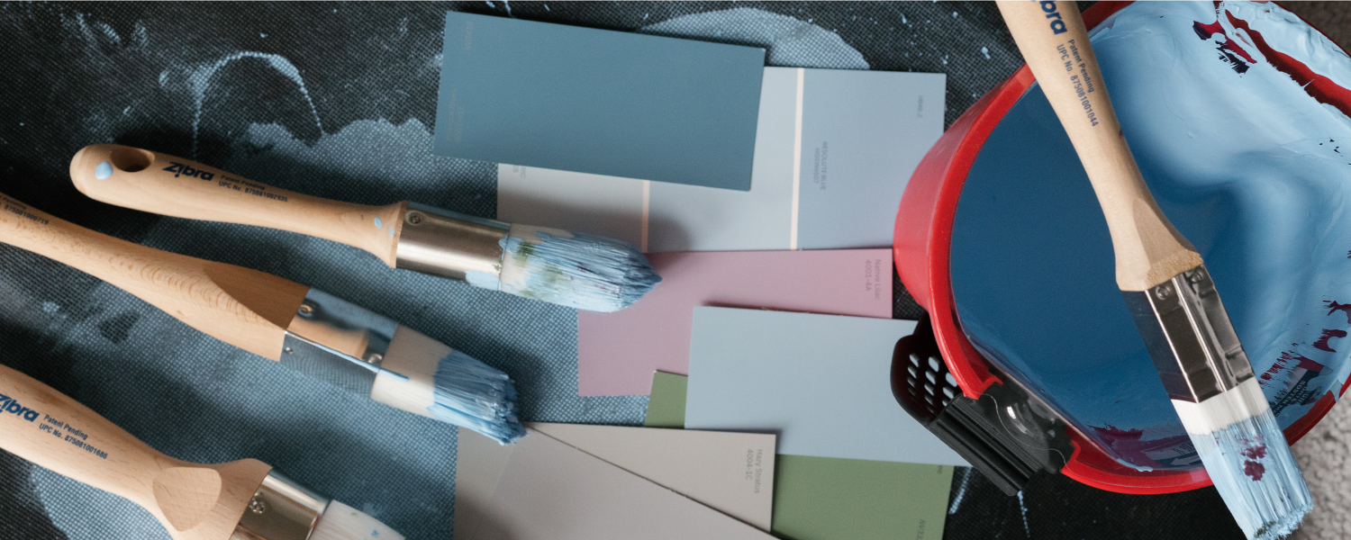 four paint brushes, paint swatches and blue paint in a handy pail